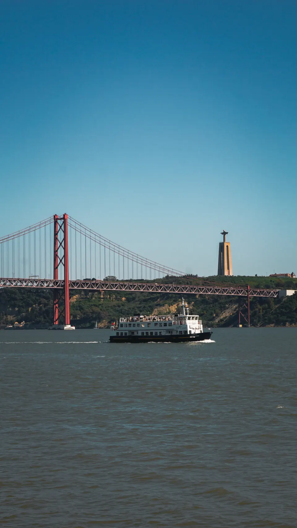 Rote Hängebrücke über den Tejo, davor eine Fähre