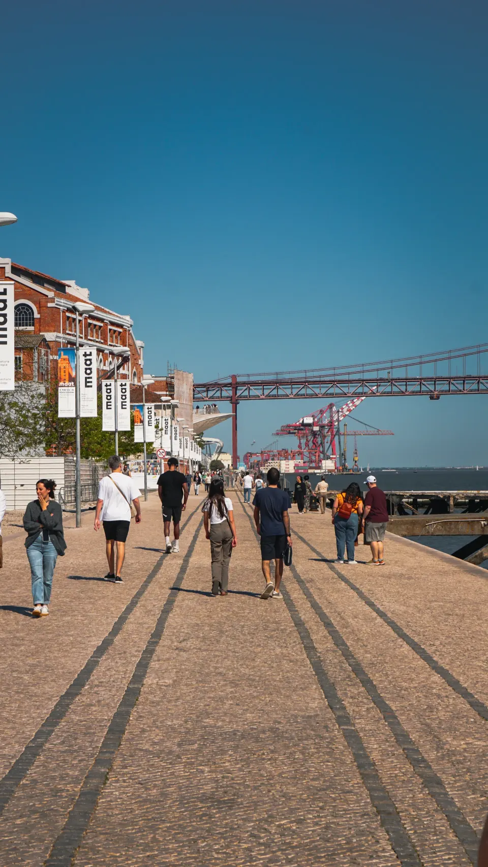 Spaziergänger auf der Uferpromenade in Lissabon, im Hintergrund die rote Brücke